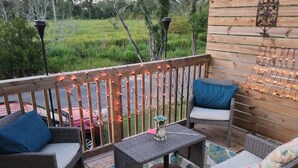 Una terraza de madera con muebles de mimbre, un tapiz estampado y luces colgantes.