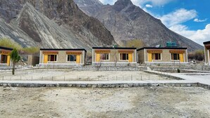 A row of traditional stone buildings with wooden doors and windows, set against a backdrop of rugged mountains. - Hunder Tamarix Resort (Leh)
