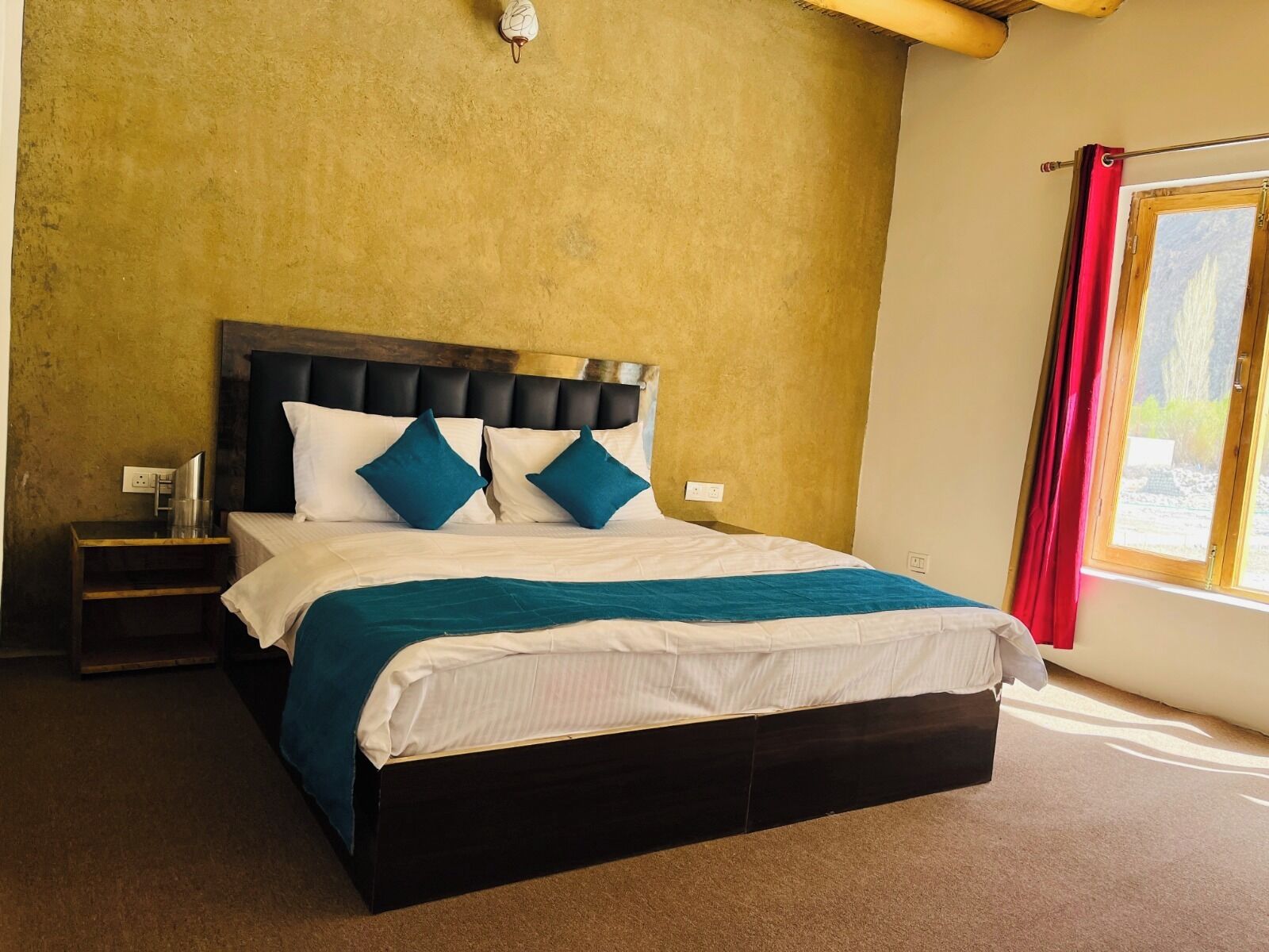A bedroom with a bed, a nightstand, a window with curtains, and a wall with a textured finish.
