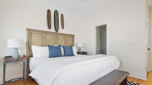 A bedroom with a large bed, two bedside tables, a bench, and a checkered rug.