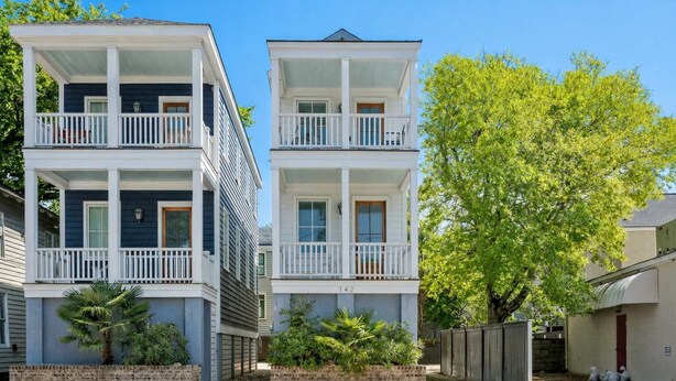 A two-story residential building with a balcony on each floor, a brick foundation, and a tree in the background.