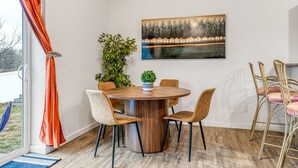 Een eethoek met een ronde houten tafel, vier stoelen, een kamerplant en een schilderij aan de muur.