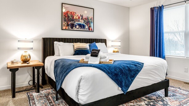 Een hotelkamer met een groot bed, een nachtkastje met lamp, een schilderij aan de muur en een raam met gordijnen.