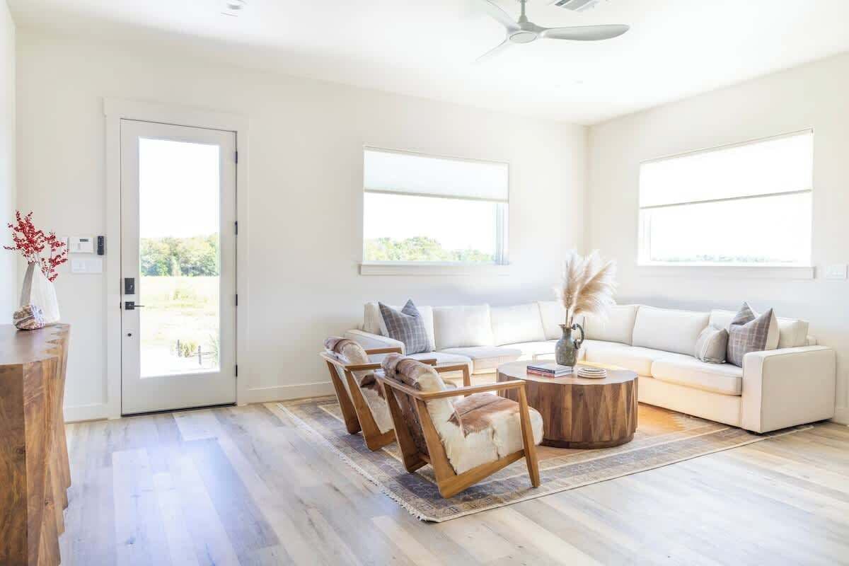 Ein geräumiges Wohnzimmer mit einem weißen Sofa, zwei Holzstühlen, einem Couchtisch und großen Fenstern, die für natürliches Licht sorgen.