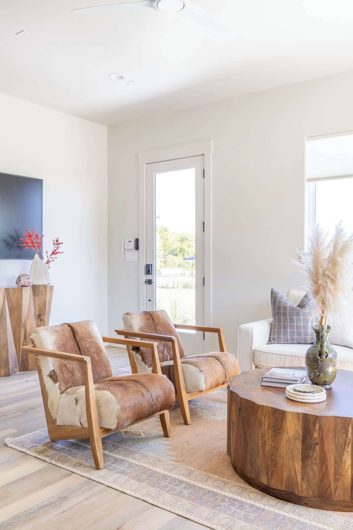 A spacious living room with a large window, a round wooden coffee table, and two leather armchairs.