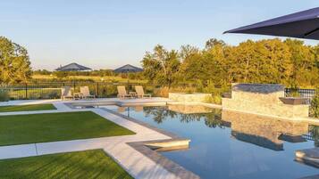 A swimming pool with lounge chairs and a stone wall, surrounded by a fence and trees.