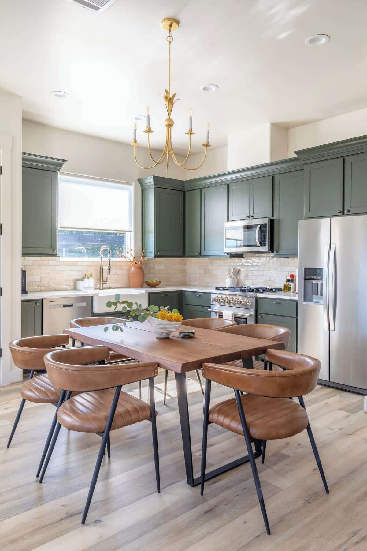 Una cocina moderna con armarios verde oscuro, electrodomésticos de acero inoxidable y una mesa de comedor de madera con sillas de cuero.