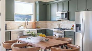 Una cocina moderna con armarios verde oscuro, electrodomésticos de acero inoxidable y una mesa de comedor de madera con sillas de cuero.