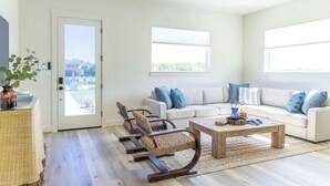 A spacious living room with a white sofa, two rocking chairs, a coffee table, and a large window. - Elevated Escape | Water Retreat @ Element Ranch (Carmine)