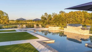 A swimming pool with lounge chairs and a stone wall, surrounded by a fence and trees. - Elevated Escape | Water Retreat @ Element Ranch (Carmine)