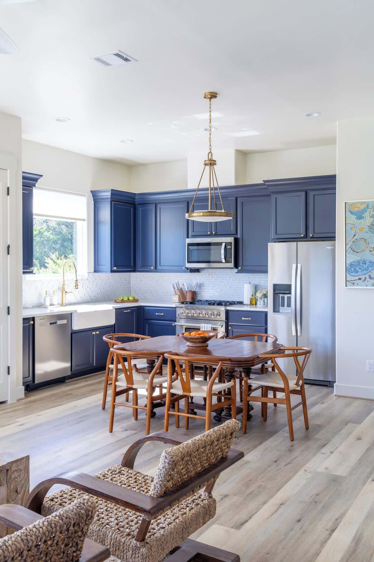 Une cuisine moderne avec des meubles de couleur bleu foncé, des appareils en acier inoxydable et une table à manger en bois, assortie de chaises.