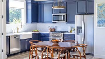 Une cuisine moderne avec des meubles de couleur bleu foncé, des appareils en acier inoxydable et une table à manger en bois, assortie de chaises.