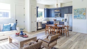 A modern kitchen with dark blue cabinets, a wooden dining table, and a hanging light fixture. - Elevated Escape | Water Retreat @ Element Ranch (Carmine)