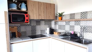 Une cuisine moderne avec des meubles en bois, un four à micro-ondes, une bouilloire et des carreaux décoratifs sur le mur derrière l’évier.