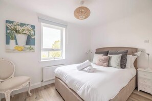 A bedroom with a bed, bedside table, chair, window, and artwork on the wall.