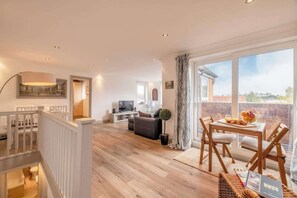 A spacious living area with a balcony, a dining table set, and a television in the background.