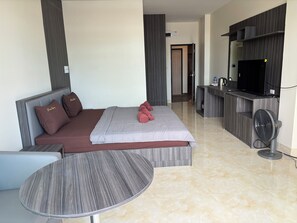 A modern hotel room with a bed, a small round table, a TV, and a kitchenette area. - new sorot house (Pattaya)
