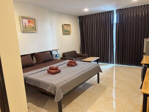 A hotel room with a bed, a sofa, a small table, and a TV. - new sorot house (Pattaya)