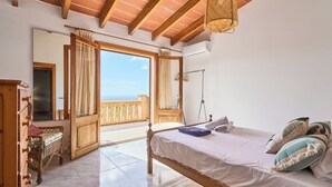 A bedroom with a bed, a wicker chair, a mirror, and a balcony with a view. - Puig de Sa Figuera Country House with Private Pool and Panoramic Views for 8 pax (Felanitx)