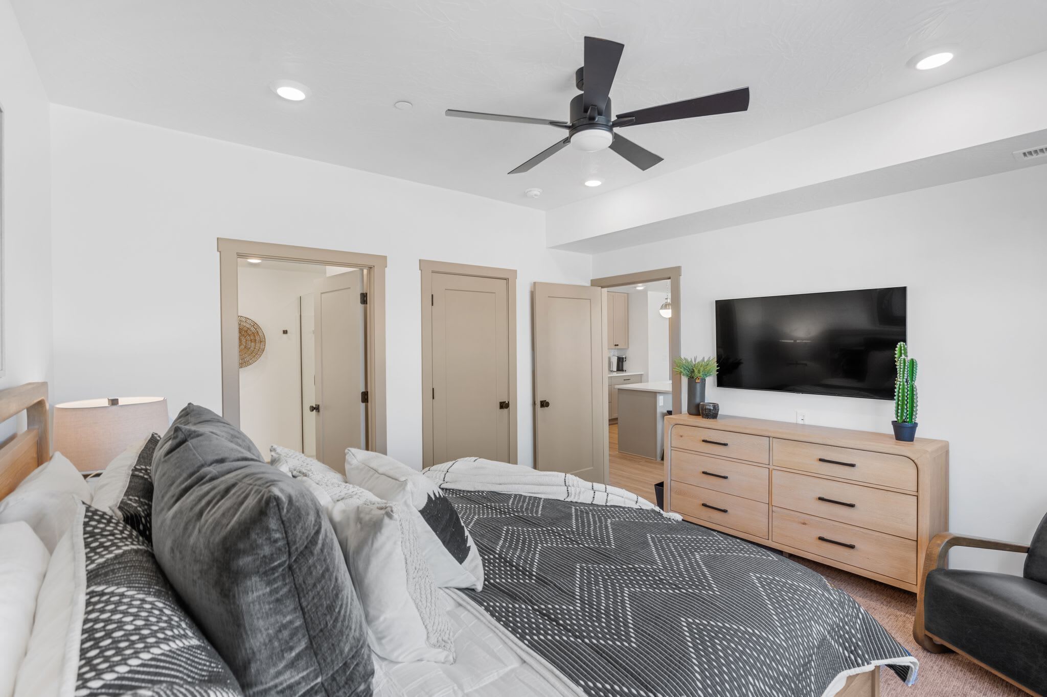 Un dormitorio moderno con cama, ventilador de techo, televisor, cómoda y silla.