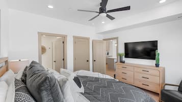 Un dormitorio moderno con cama, ventilador de techo, televisor, cómoda y silla.