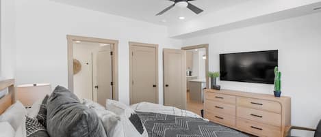 Une chambre à coucher moderne, avec un lit, un ventilateur de plafond, une télévision, une commode et une chaise.