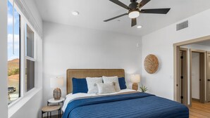 A bedroom with a large bed, a ceiling fan, a window with a view of the desert, and a door to another room.
