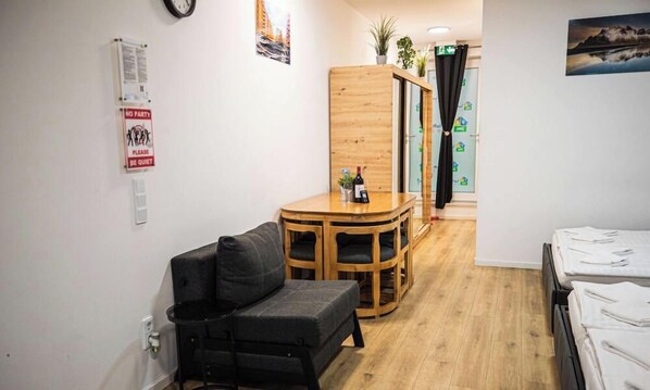 A small, furnished room with a sofa, a wooden table, and a bed with neatly made sheets.