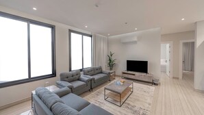 A modern living room with a grey sectional sofa, a coffee table, and a flat-screen TV. - Mabaat - Al Rimal - 565 (Riyadh)