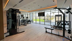 A spacious gym with various exercise equipment, large windows, and a flat-screen TV. - Modern 2 Bed with Stunning Views (Dubai)