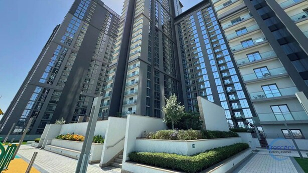 A high-rise residential building with multiple balconies, a clear sky, and a well-maintained garden area. - Modern 2 Bed with Stunning Views (Dubai)
