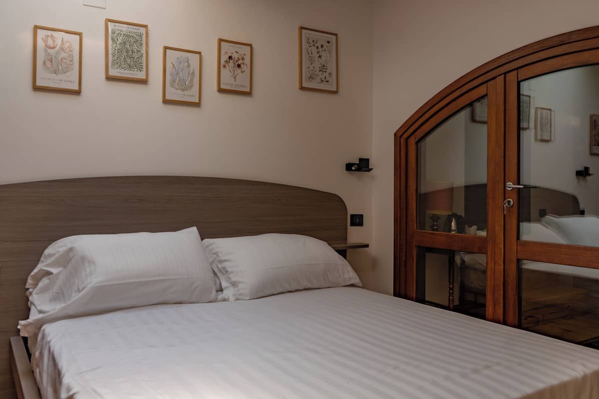 A neatly made bed with white linens, a wooden headboard, and four framed botanical prints on the wall.