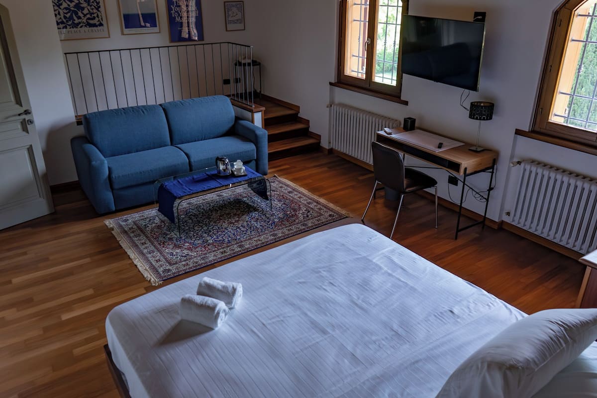 A bedroom with a bed, a blue sofa, a desk, and a TV.