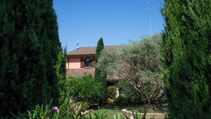A house with a tiled roof, surrounded by dense evergreen trees and a well-maintained garden.