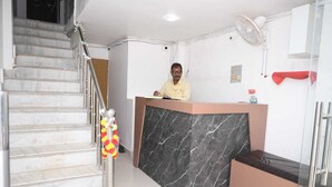 A reception desk with a marble counter, a staircase with a decorative garland, and a fan on the wall. - VIP Paying Guest House (Varanasi)