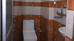 A small, compact bathroom with a toilet, a sink, and a shower. - VIP Paying Guest House (Varanasi)