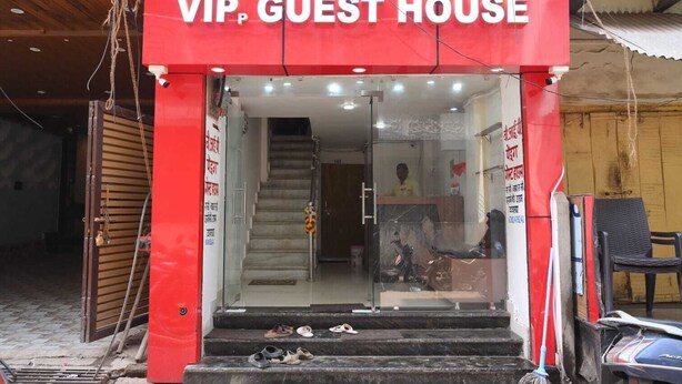 The entrance to a VIP Guest House with a red facade, a reception desk inside, and a staircase leading to the entrance. - VIP Paying Guest House (Varanasi)