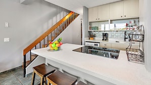 A modern kitchen with a white countertop, stainless steel appliances, and a wooden staircase.