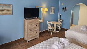 Habitación de hotel con cómoda de madera, televisor, escritorio y dos sillas, y una cama.