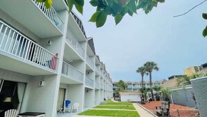 Un hotel de varios pisos con balcones, un camino de césped y palmeras.