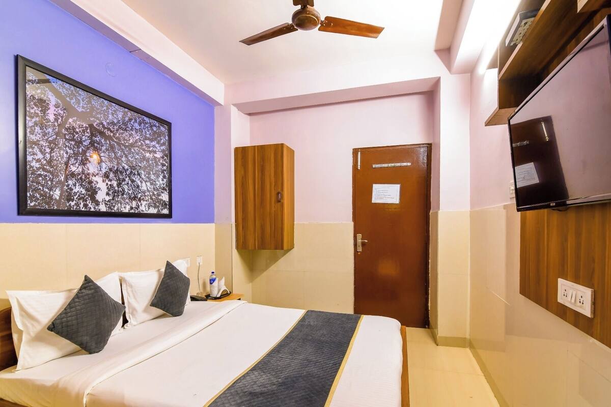 A hotel room with a bed, a ceiling fan, a wardrobe, a door, and a wall-mounted TV.