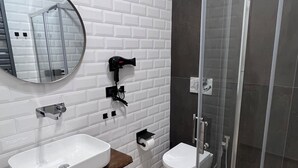 Een moderne badkamer met een wand betegeld met witte metrotegels, een ronde spiegel, een witte wasbak, een toilet en een douche met glazen wanden.