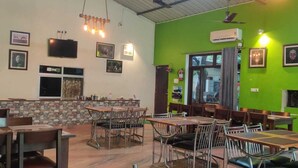 Un ristorante con una parete verde, tavoli e sedie in legno, un bancone in pietra e quadri appesi al muro.