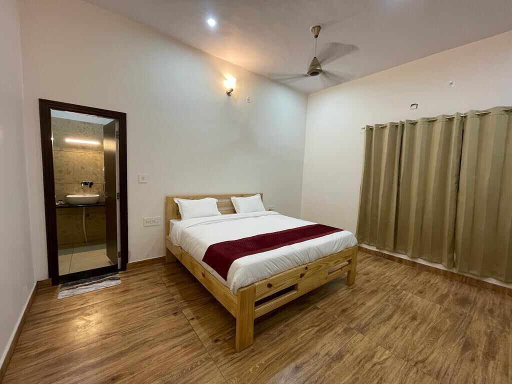 A bedroom with a wooden bed, a ceiling fan, a bathroom with a mirror, and a window with curtains.