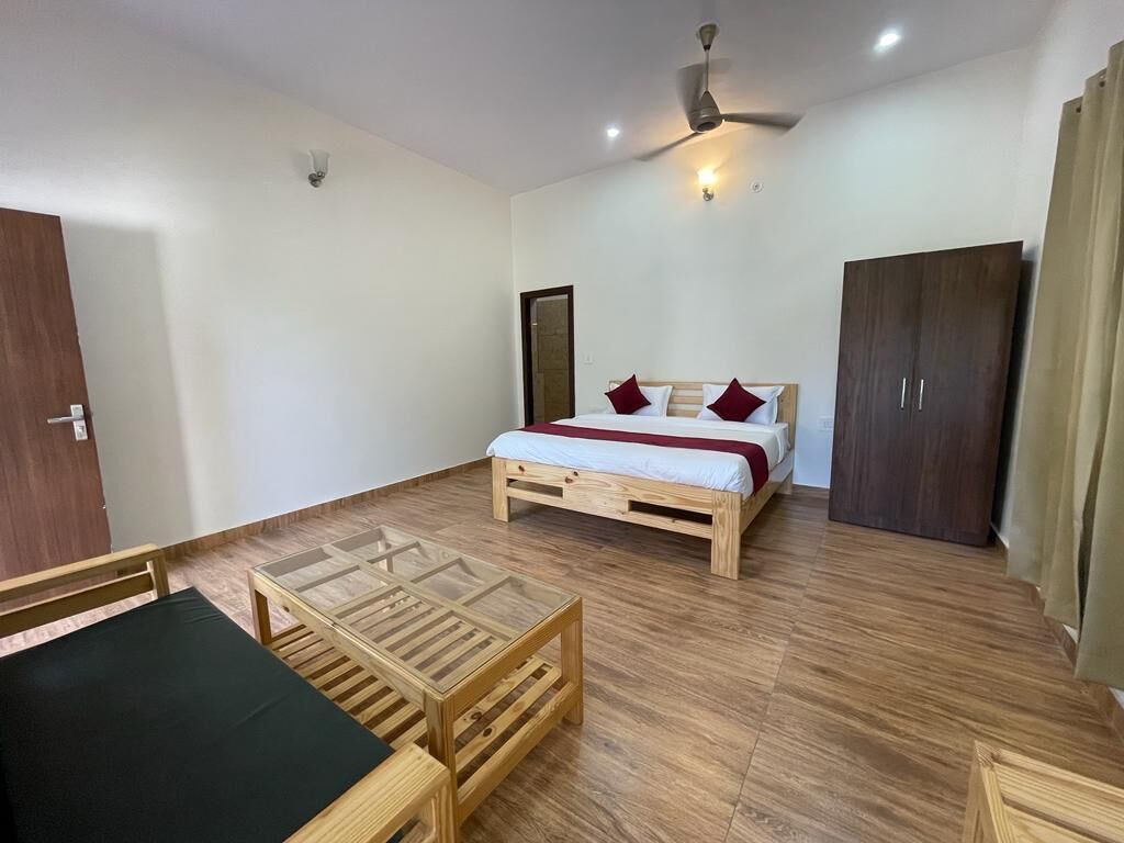 A room with a bed, a wooden table, a ceiling fan, and a wardrobe.