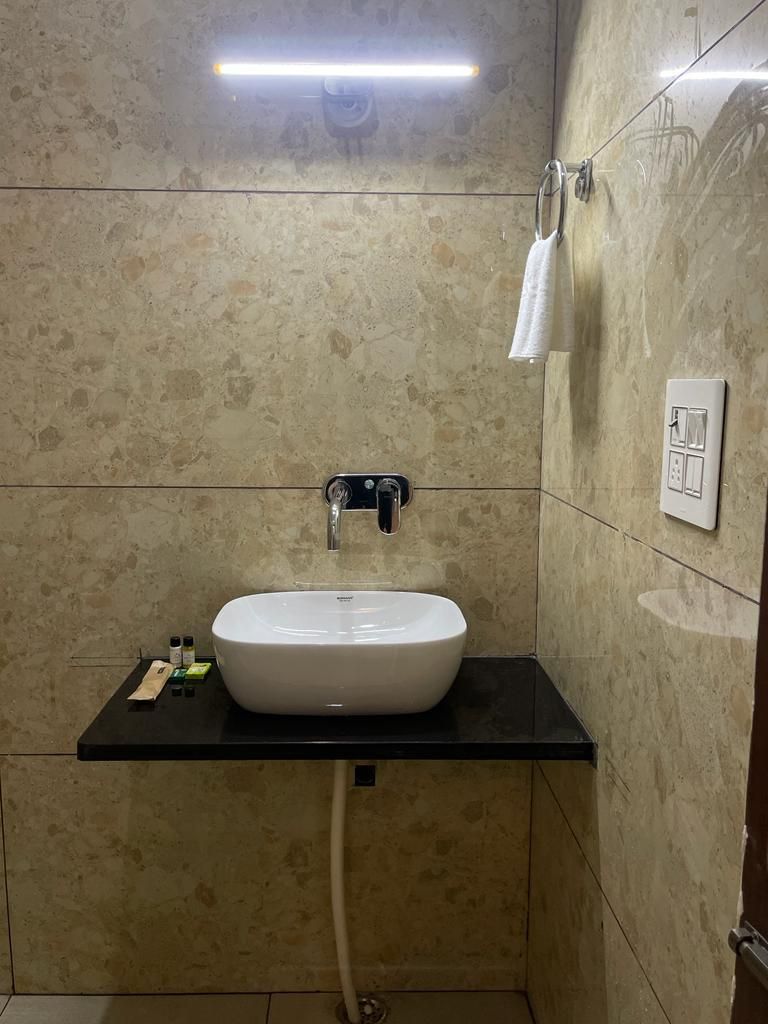 Une salle de bain avec un lavabo blanc, un plan de toilette noir et des murs recouverts de carreaux beiges.