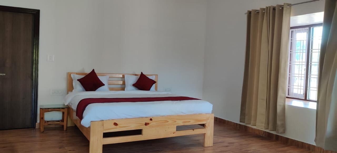 A wooden bed with a white mattress and red pillows, a wooden nightstand, and a window with curtains.