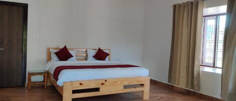 A wooden bed with a white mattress and red pillows, a wooden nightstand, and a window with curtains.