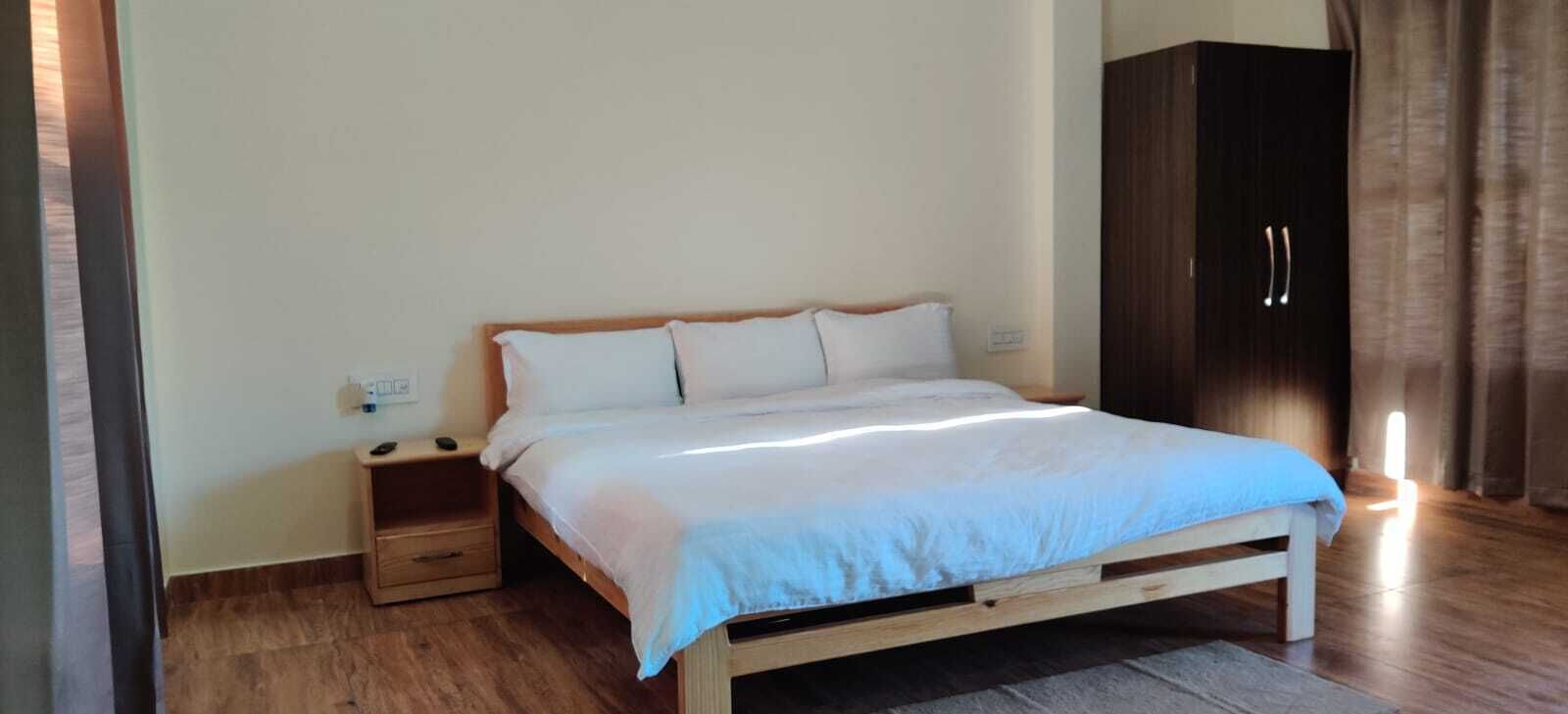Une chambre à coucher avec un lit en bois, du linge de lit blanc, une table de chevet, une armoire et une petite commode.