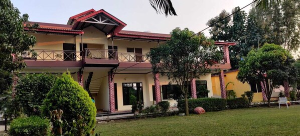 A two-story building with a balcony, surrounded by lush greenery.